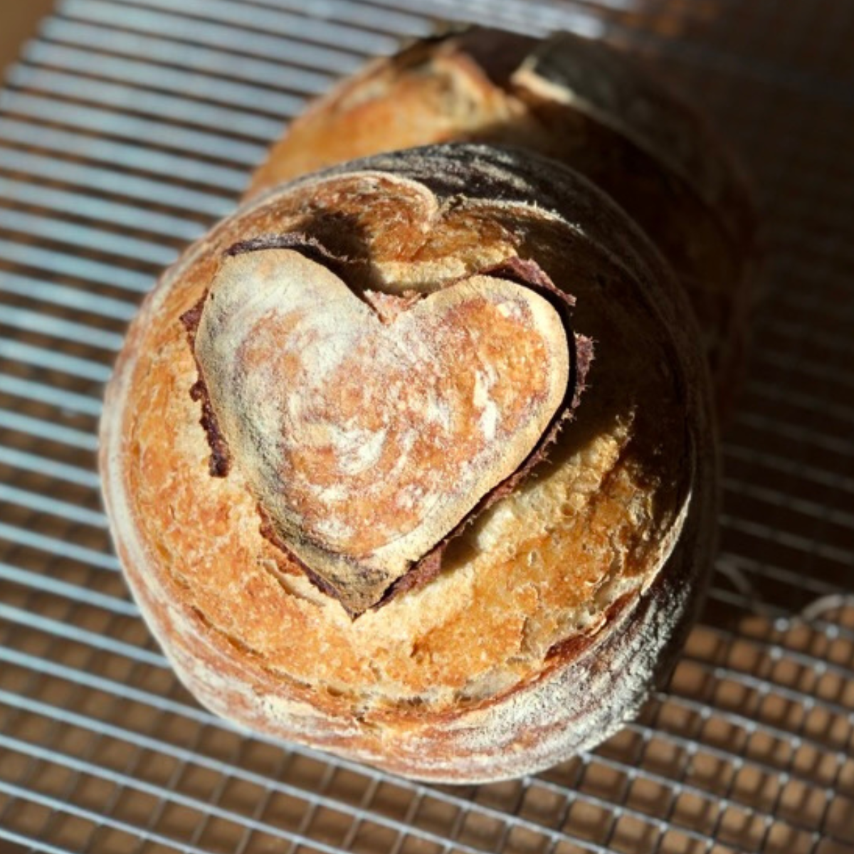 image of two round boules of sourdough bread scored with a heart on a cooling rack
