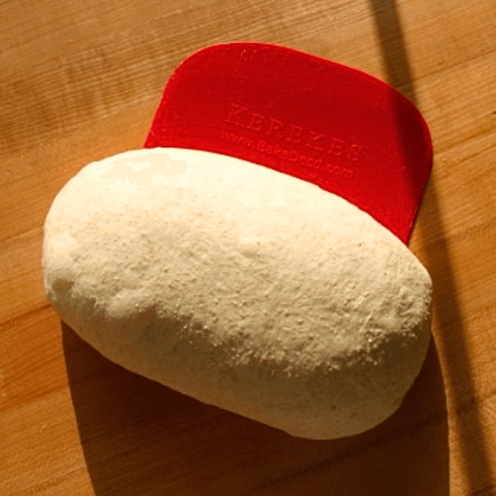 shaped sourdough sandwich loaf dough with red dough scraper on a wood table
