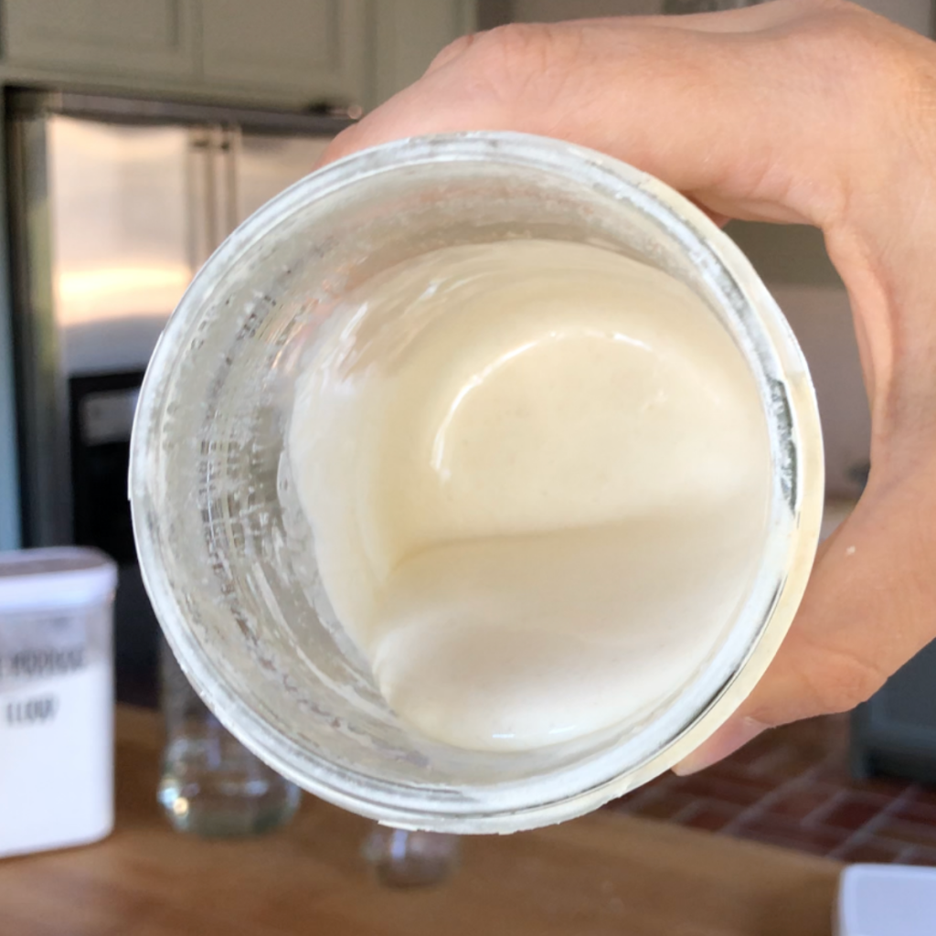 image of hand holding jar of sourdough discard showing inside of jar in a kitchen