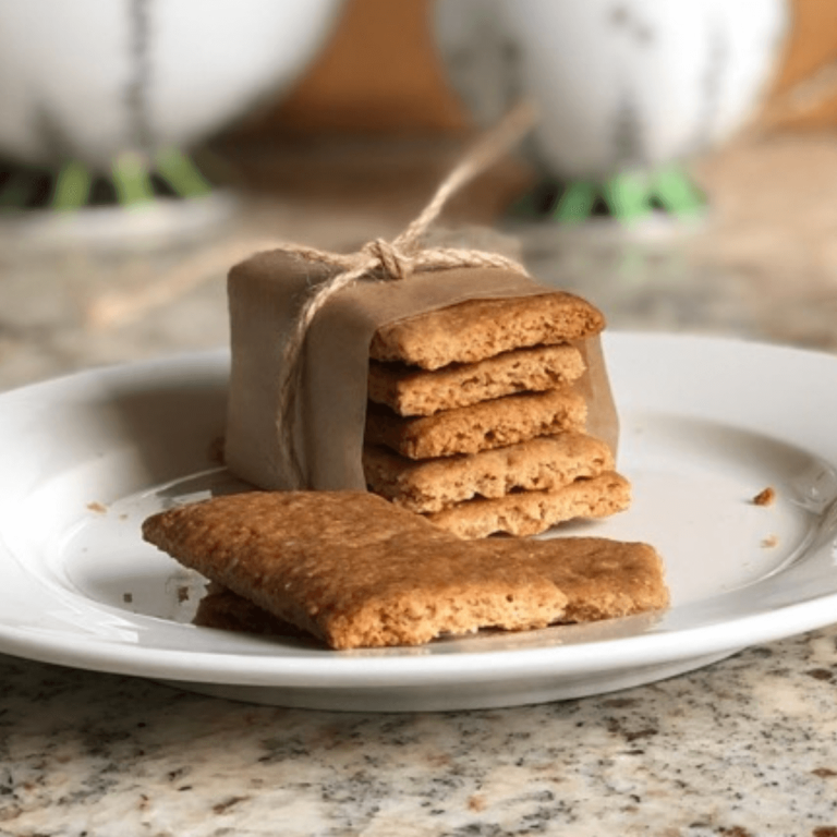 bundle of stacked sourdough graham crackers on a white plate on a granite counter in kitchen with white and green teapot in the background