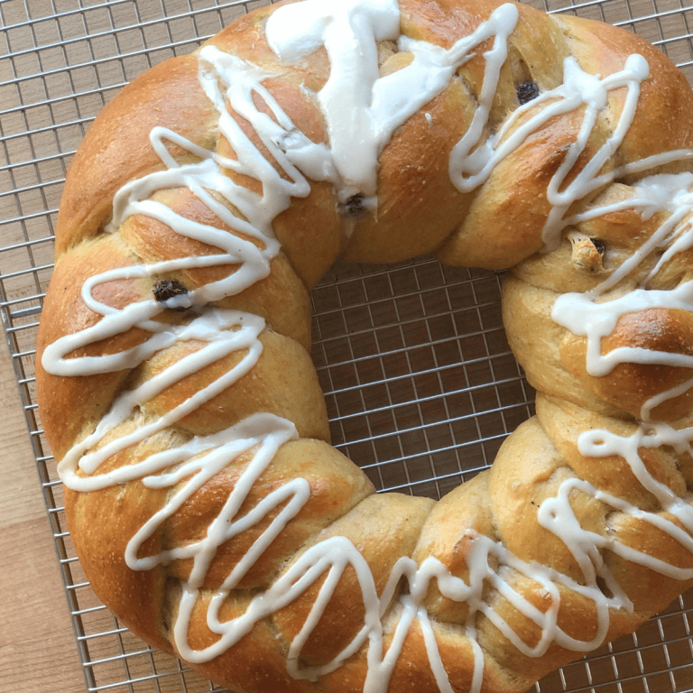 sourdough hot cross wreath bread on a cooling rack decorated with white icing drizzled in zig zags with a cross at the top