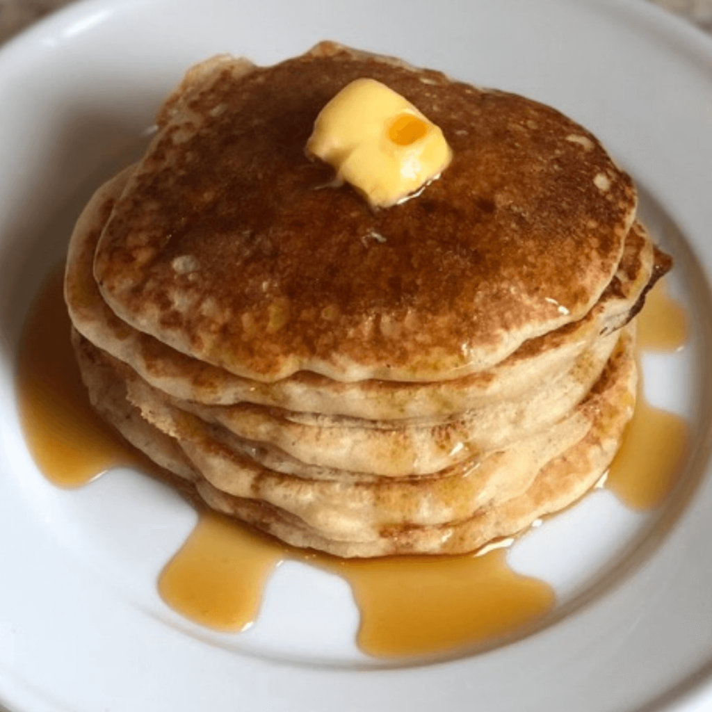 stack of sourdough pancakes topped with a square of butter and maple syrup on a white plate