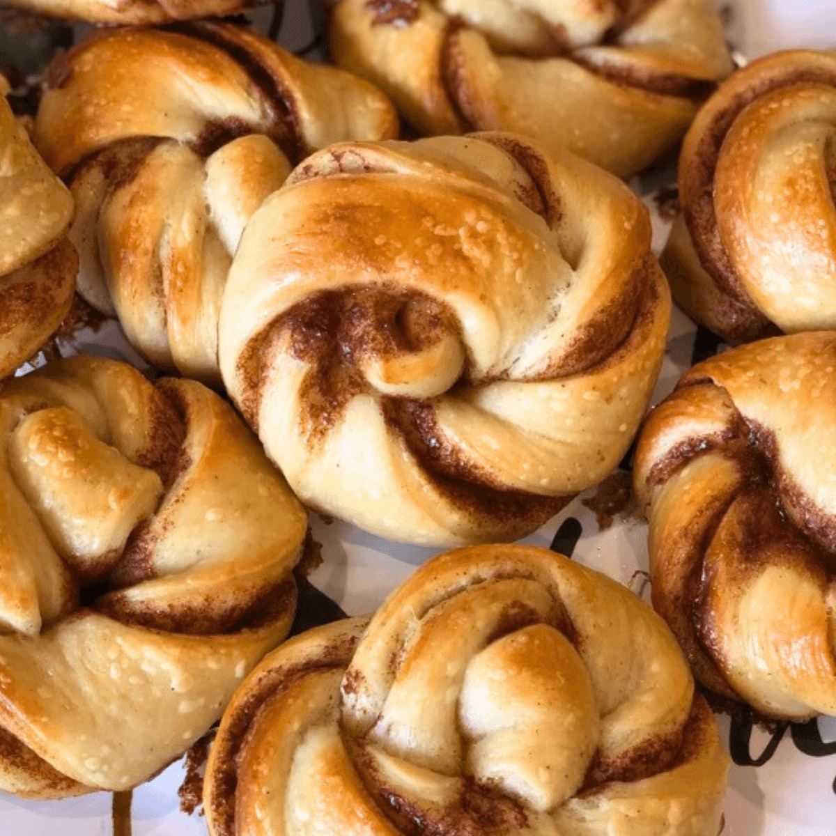 An assortment of Swedish cinnamon roll twisted knots known as kanelbullar on a platter. Shown are sourdough kanelbullar