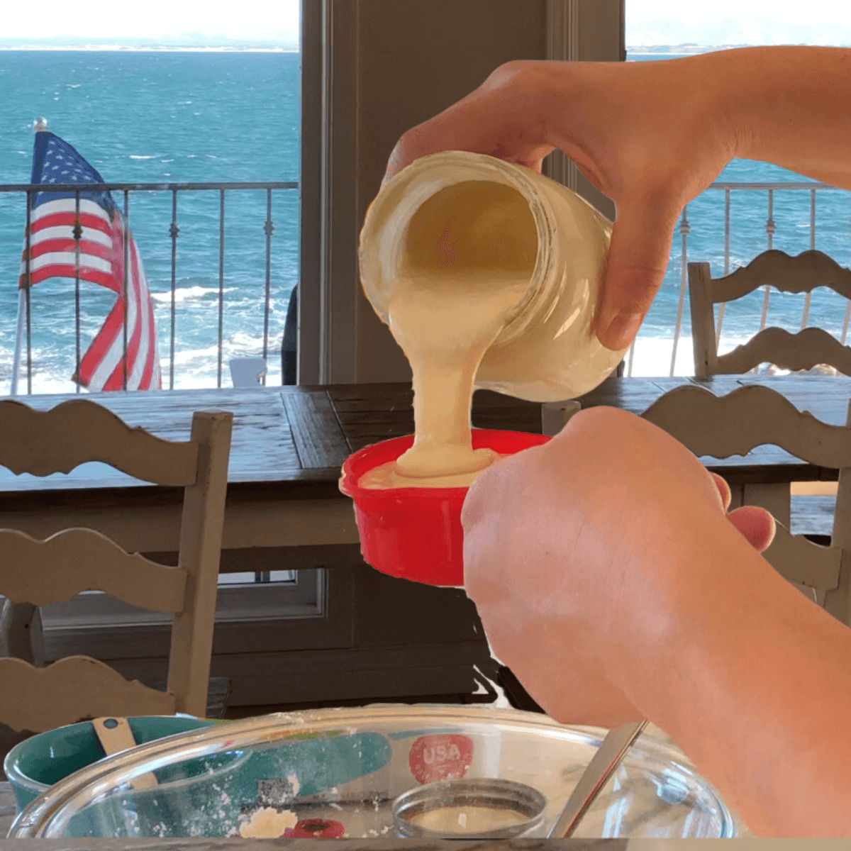 woman's hands pouring a jar of sourdough starter discard into a measuring cup with an ocean view in the background