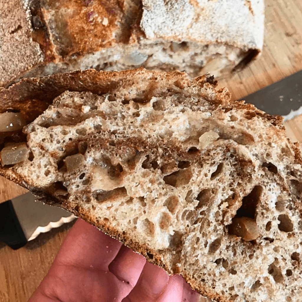 hand holding a slice of Sourdough Apple Cinnamon Spice Country Bread cut from a loaf