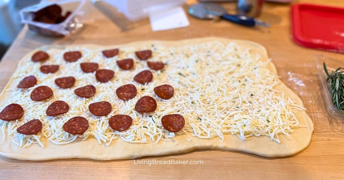 easy sourdough pizza rolls with dough rolled out topped with grated cheese and pepperoni slices